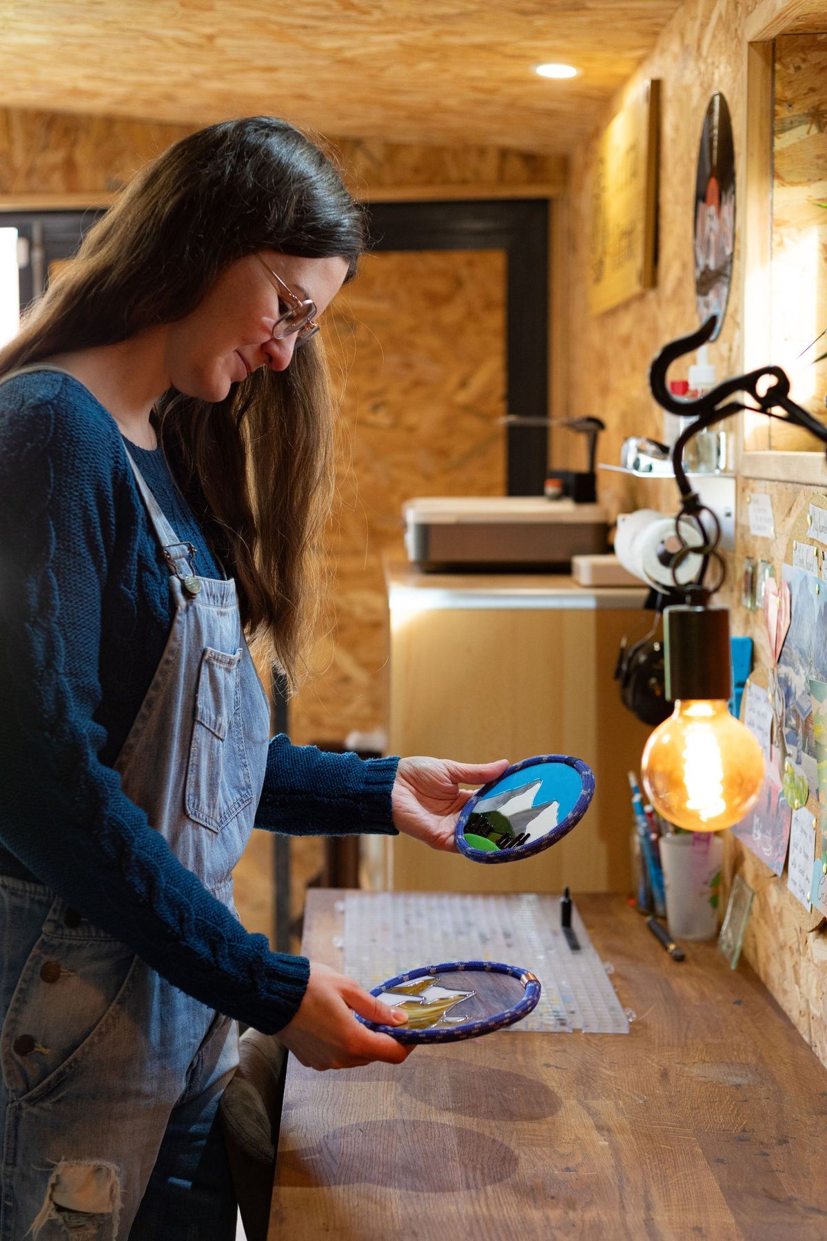 Terra Vitrae - Décorations en vitrail et verre fondu et bois, inspirées de la nature et la montagne - L'artisane et 2 décorations murales dans son atelier