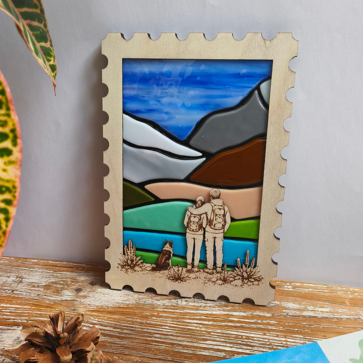 Décoration murale artisanale - paysage montagne en verre fondu - cadre en bois en forme de timbre – couple de randonneurs avec leur chien gravés dans le bois. 